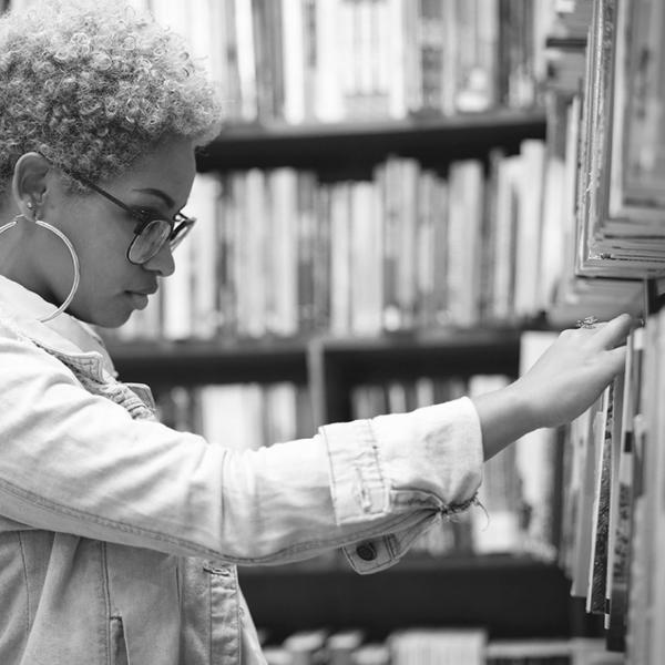 Black woman student pulling a book off a library shelf