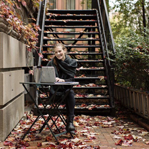 Young woman working on a laptop outside on a fall day